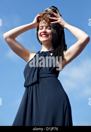 Portrait mi-shot d'une femme souriant et tenant son foulard contre le ciel bleu, Londres, Angleterre, Royaume-Uni. Banque D'Images