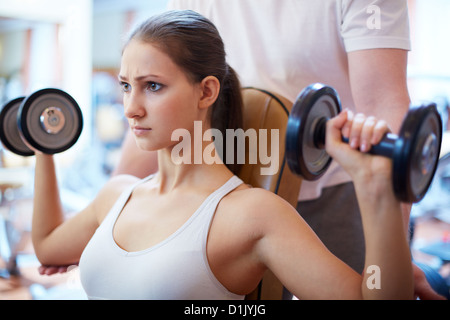 Portrait de jolie fille de la formation en salle de sport avec son entraîneur derrière l'aidant Banque D'Images