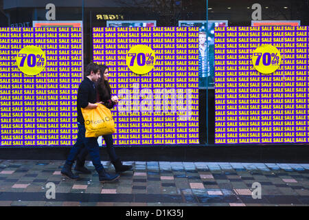 Le mercredi 26 décembre 2012. Le lendemain de la vente, Glasgow, Écosse. Jeune homme et la jeune femme en passant devant une vitrine d'une vente de la publicité jusqu'à 70 % de réduction. Banque D'Images