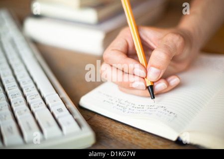 Photo de mains écrit un stylo dans un ordinateur portable, clavier de l'ordinateur et une pile de livres en arrière-plan Banque D'Images