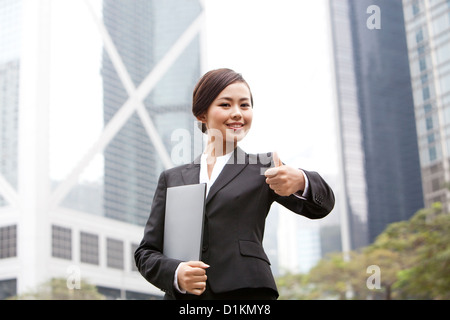 Happy businesswoman doing Thumbs up avec portfolio en main, Hong Kong Banque D'Images