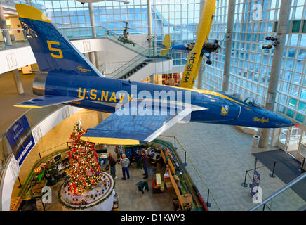 26 déc 2012 - Garden City, New York, États-Unis - le Long Island Garden Railway Society modèle à grande échelle de train entoure un grand arbre décoré pour une ambiance festive de vacances hiver attraction dans le vaste atrium de berceau de l'Aviation Museum. LIGRS partage les connaissances, fun, et la camaraderie de l'exploitation ferroviaire à grande échelle à l'intérieur et dans le jardin, et est axée sur la famille. Un bleu et jaune restauré Grumman F-11A Tiger jet, U.S. Navy, est suspendu au plafond de l'étage 3 atirum. Banque D'Images