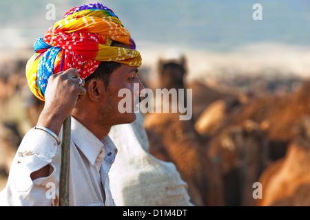 Un commerçant d'une chamelle turban lumineux semble songeur à chameaux au cours de l'assemblée juste chameau à Pushkar Rajasthan Inde Asie Banque D'Images