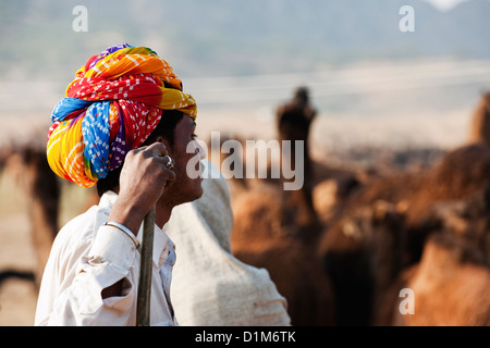 Un commerçant d'une chamelle turban lumineux semble songeur à chameaux au cours de l'assemblée juste chameau à Pushkar Rajasthan Inde Asie Banque D'Images