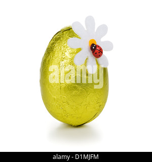 Bonbons au chocolat oeuf de Pâques enveloppés dans une feuille d'or décoré de fleur et coccinelle sur fond blanc Banque D'Images