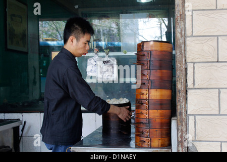 Un homme chinois cuisine chinoise traditionnelle des dim sum (raviolis chinois) dans des paniers vapeur en bambou Banque D'Images