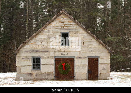 Couronne de Noël décore une porte en bois d'une ancienne grange en pierre dans une scène de Noël avec la neige qui tombe dans la Nouvelle Angleterre. Banque D'Images