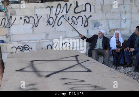 1 janvier 2013 - Hébron, en Cisjordanie, territoire palestinien - les Palestiniens s'asseoir près d'un mur pulvérisé avec graffiti écrit en hébreu dans le village de Beit Omar, au nord de la ville de Cisjordanie d'Hébron, le 1er janvier 2013. Vandales que l'on croit être des extrémistes juifs light (pour une voiture dans le village et griffonné des graffitis racistes sur un mur proche, palestiniens et israéliens a dit. Le Graffiti se lit en hébreu, ''Prix'', ''un bon arabe est un Arabe mort'', ''Aujourd'hui dans l'immobilier, demain -- Vie,'' et ''La vengeance de Yitzhar (un règlement dans le nord de la Cisjordanie (crédit Image : © Mamoun Wazwaz Images/APA/ZU Banque D'Images