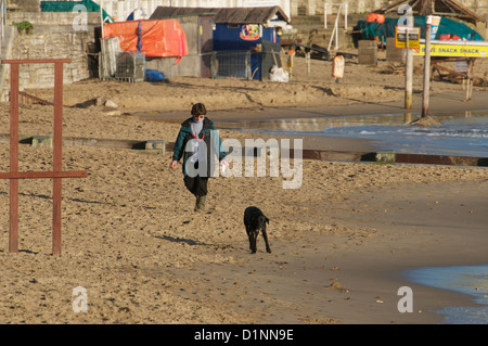 Femme entre chien sur la plage de Swanage dans winter sunshine Banque D'Images