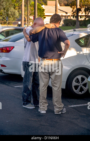 Bras dessus bras dessous, deux hommes prier ensemble dans une Laguna Niguel, CA, un parking. Banque D'Images