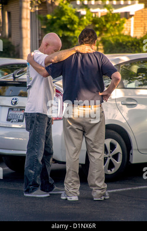 Bras dessus bras dessous, deux hommes prier ensemble dans une Laguna Niguel, CA, un parking. Banque D'Images