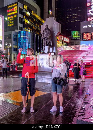 À l'aide de caméras Smartphone, deux jeunes touristes adultes photographie Times Square, New York City sur une nuit pluvieuse. Banque D'Images