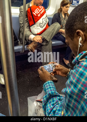 Un African American man joue un jeu vidéo sur un smartphone tout en équitation dans le New York City subway. Banque D'Images