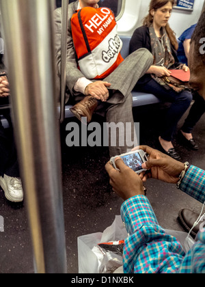 Un African American man joue un jeu vidéo sur un smartphone tout en équitation dans le New York City subway. Banque D'Images