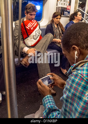 Un African American man joue un jeu vidéo sur un smartphone tout en équitation dans le New York City subway. Banque D'Images