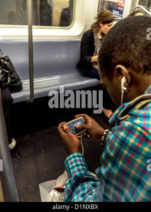 Un African American man joue un jeu vidéo sur un smartphone tout en équitation dans le New York City subway. Banque D'Images