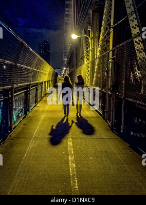 Deux jeunes femmes à pied à travers la ville de New York Manhattan Bridge at night. Banque D'Images