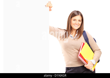 A smiling female student debout à côté d'un panneau blanc isolé sur fond blanc Banque D'Images