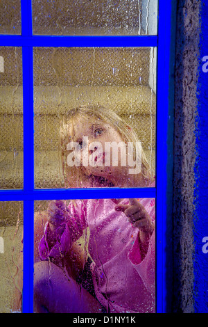 Une fillette de cinq ans, regarde par sa fenêtre, la nuit dans la banlieue de Lake Forest, CA. Banque D'Images