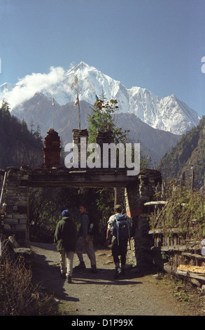 Les randonneurs à pied à travers la porte d'entrée porche pour village sur le circuit de l'Annapurna dans l'Himalaya au Népal avec neige snow clad peak Banque D'Images