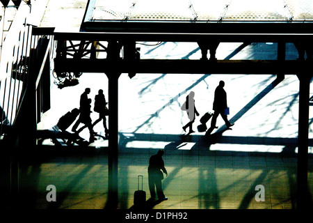 Les voyageurs arrivant à l'aéroport d'Heathrow, Terminal 5, en silhouette, marche à pied avec leurs bagages Banque D'Images