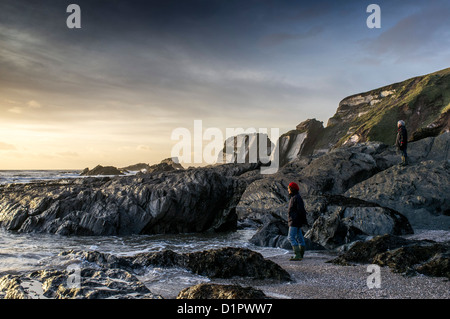 Un Couple regardant le soleil d'hiver se coucher sur la mer de la plage. Ayrmer Cove, Devon. ROYAUME-UNI Banque D'Images