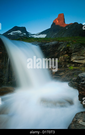 Cascade dans la vallée de Vengedalen et début de matinée alpenglow sur le pic de Romsdalshorn, 1550 m, à Rauma kommune, Møre og Romsdal, Norvège, Scandinavie. Banque D'Images