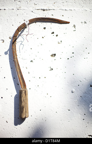 Old rusty scythe accrochée à un mur ensoleillé Banque D'Images