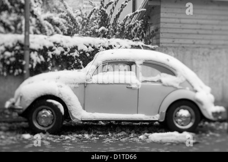 Le noir et blanc tilt shift droit d'une vieille Volkswagen Bugs se trouve dans une rue couverte de neige en Europe. Banque D'Images