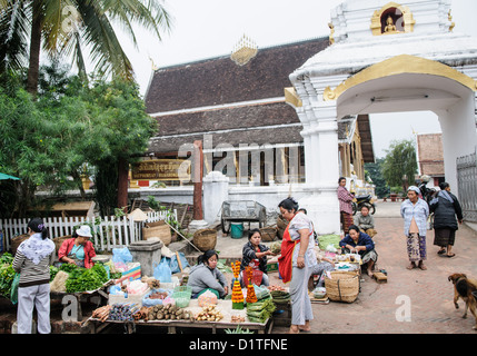 Marché du matin près de Wat Phonxay Sanasongkham Luang Prabang Laos // LUANG PRABANG, Laos — les vendeurs du marché organisent leurs stands près de Wat Phonxay Sanasongkham au petit matin. Le marché quotidien attire les habitants et les visiteurs, offrant des produits frais et des produits traditionnels essentiels à la cuisine lao. Wat Phonxay Sanasongkham est l'un des temples bouddhistes de Luang Prabang, une ville classée au patrimoine mondial de l'UNESCO et connue pour préserver l'architecture et la culture traditionnelles lao. Le marché représente la continuation de traditions commerciales séculaires dans cette ancienne capitale royale. Luang Prabang Banque D'Images