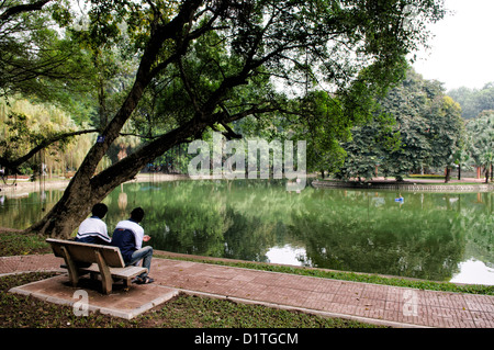 HANOI, Vietnam — deux jeunes hommes sont assis sur un banc surplombant un petit lac dans les jardins botaniques de Hanoi (Vuon Bach Thao). Banque D'Images