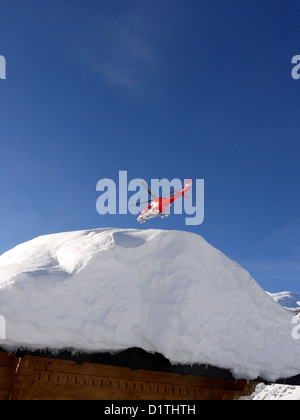 Rega Swiss Mountain Rescue hélicoptère survolant un toit chalet laden avec snow Banque D'Images