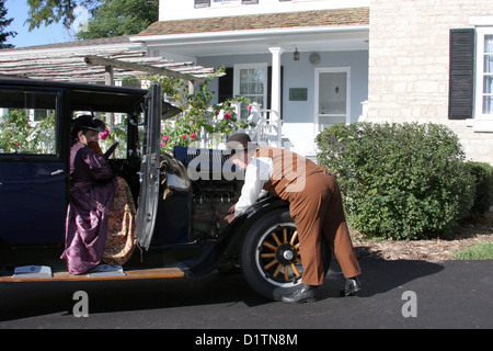 Un homme d'essayer de réparer un 1925 Dodge Brothers automobile qui n'est pas partir alors qu'une dame attend Banque D'Images