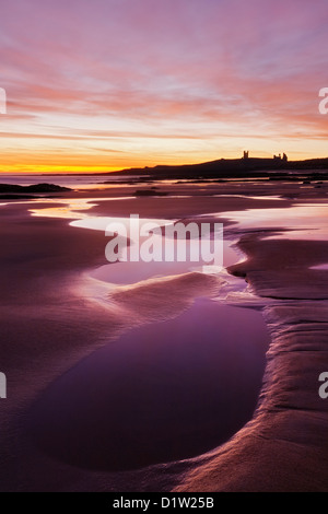 Vue le long de la baie au lever du soleil avec Embleton silhouette de Château de Dunstanburgh au loin, près de Alnwick, Northumberland Royaume-uni Banque D'Images