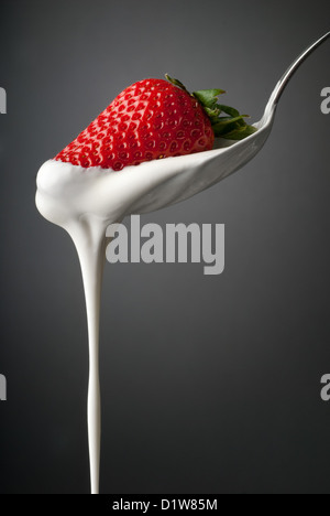 Filet de crème fouettée une cuillère en argent avec une fraise rouge Banque D'Images