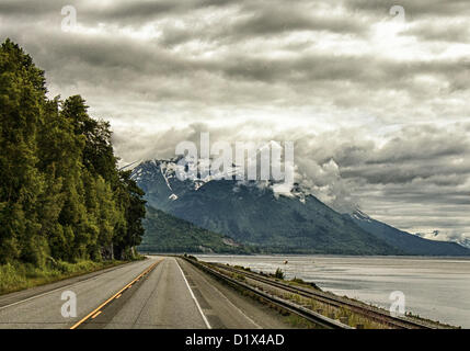 29 juin 2012 - péninsule de Kenai, Alaska, Etats-Unis - conduite au sud, pittoresque Seward Highway longe la base de la montagnes Chugach et offre des vues spectaculaires sur les glaciers, montagnes aux montagnes Kenai encadrée par les formations de nuages spectaculaires. Ils s'élèvent au loin au-dessus de Turnagain Arm, à marée basse, ses eaux juste couvrant la baie. À droite, l'Alaska Railroad tracks longent la route. Une forêt nationale désignée Scenic Byway, un All-American Road et un Scenic Byway, l'ALASKA Seward Highway exécute 127 miles [204 km] de mouillage à Seward à travers la péninsule Kenai Chugach State Park, Banque D'Images