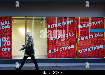 Motion blurred femme passant affiches des réductions dans la fenêtre de Primark, Bromley. Banque D'Images