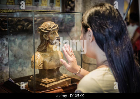 Femme priant devant une statue du Christ à l'intérieur de la Basilica Minore del Santo Niño, Cebu, Philippines Banque D'Images