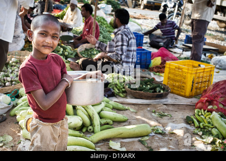 Pauvre jeune garçon des rues indiennes transportant des pots en face d'un marché de rue. L'Andhra Pradesh, Inde Banque D'Images