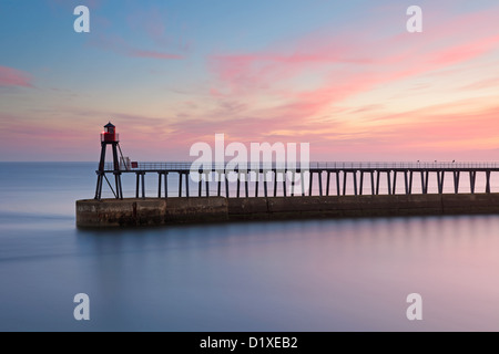 La jetée est dans le port de Whitby, North Yorkshire. Pris au lever du soleil que le soleil illumine le ciel avec des tons de rose. Banque D'Images