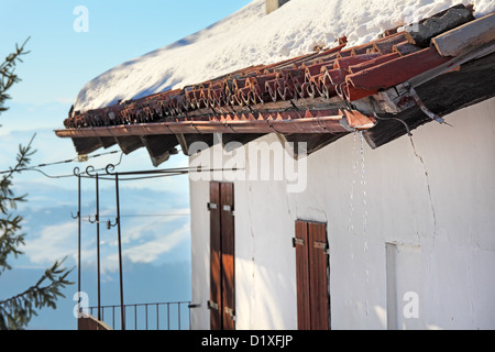 La fonte de la neige sur le toit de tuiles rouges sur balcon et volets en bois. Banque D'Images