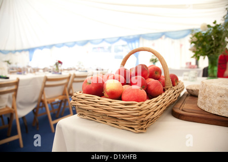 Panier de pommes rouges sur une table à côté des fromages, des tables et chaises pour une réception de mariage dans un rectangle en arrière-plan Banque D'Images