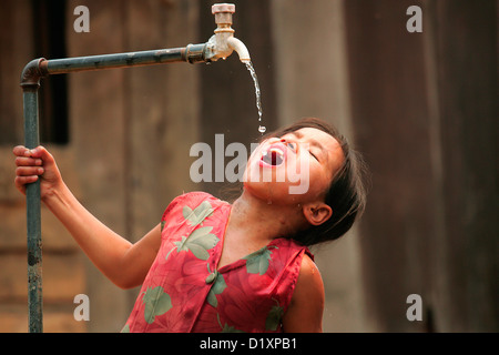 Une jeune fille des boissons à partir d'un robinet dans le village de Baw sur le Mékong près de Luang Prabang, Laos, Nord, Sud-Est, l'Asie. Banque D'Images