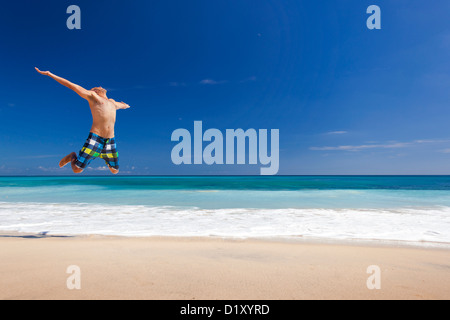 Jeune homme athlétique jouissant de l'été, sauter dans une plage tropicale Banque D'Images