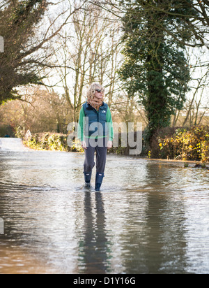 Woman in wellies marcher dans les eaux d'inondation sur une route du Warwickshire Banque D'Images