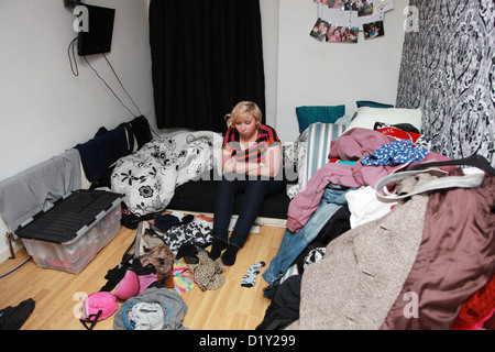 Déprimé girl sitting on lit dans sa chambre en désordre Banque D'Images