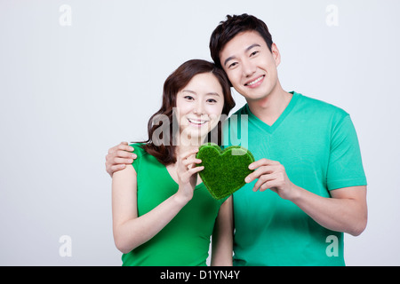 Un couple en vert t-shirts tenant un cœur, la figure fait de l'herbe Banque D'Images