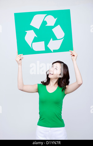 Une femme en t-shirt vert à la recherche jusqu'à son logo de recyclage pancarte Banque D'Images