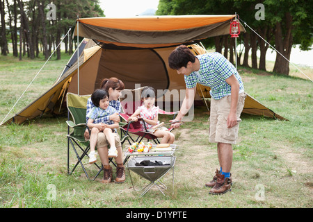 Cuisson tandis que le père d'autres membres de la famille assis sur chaises de camping Banque D'Images