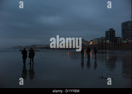 Les gens qui marchent sur la plage, à marée basse, West Pier de Brighton, UK, dusk Banque D'Images